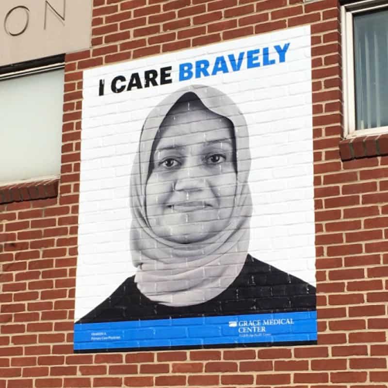 outdoor vinyl graphic signage on brick featuring woman saying she cares bravely